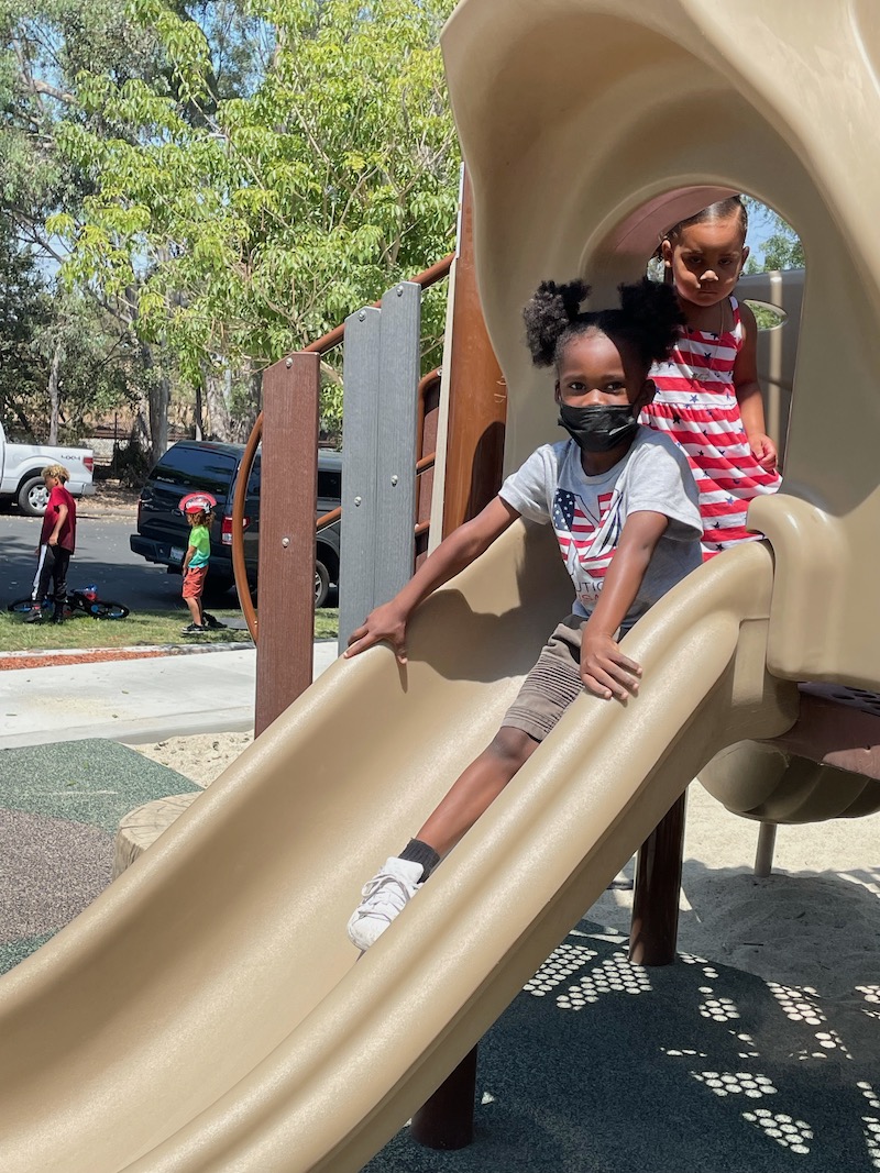 A little girl is waiting for her turn on the slide after her friend goes down it.