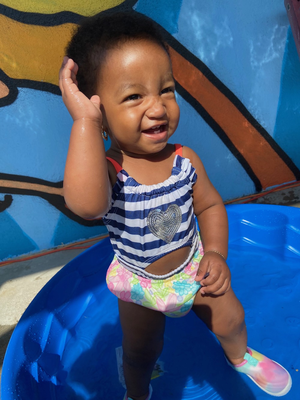 Baby girl standing in the pool smiling.