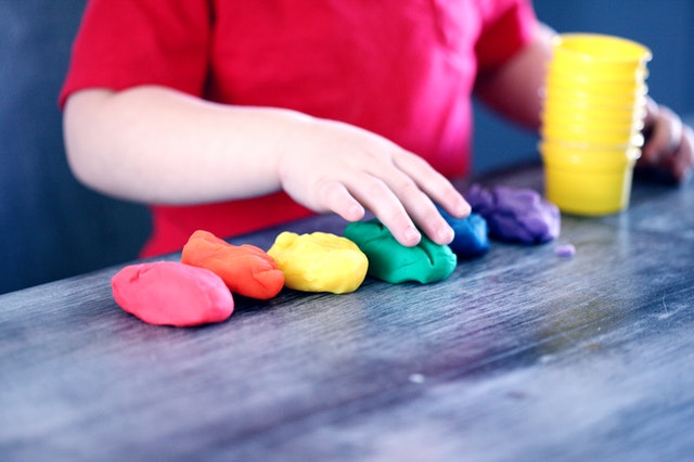 A little boy is standing at a desk playing with Play-Doh.