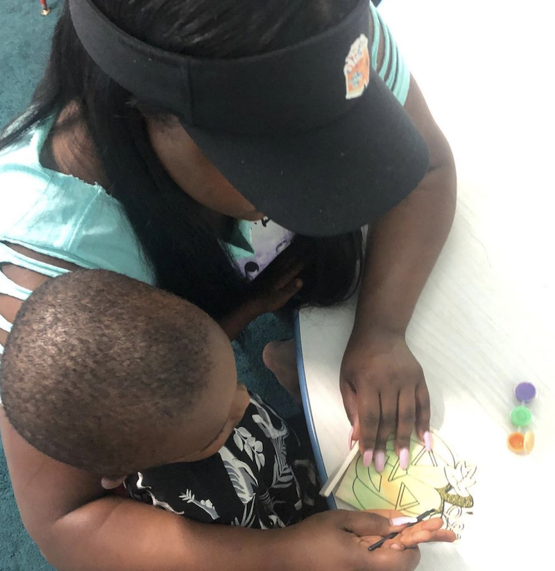 Teacher helping a child hold a paint brush to paint a Halloween picture.