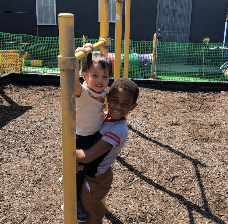 A little boy is holding another so he can reach the bar at the jungle gym.
