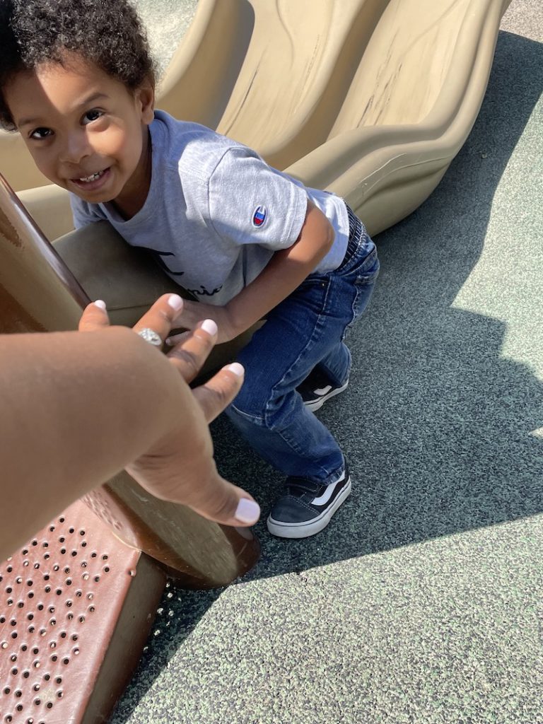 Ms. Tee is holding out her hand to help a little boy get on the slide.