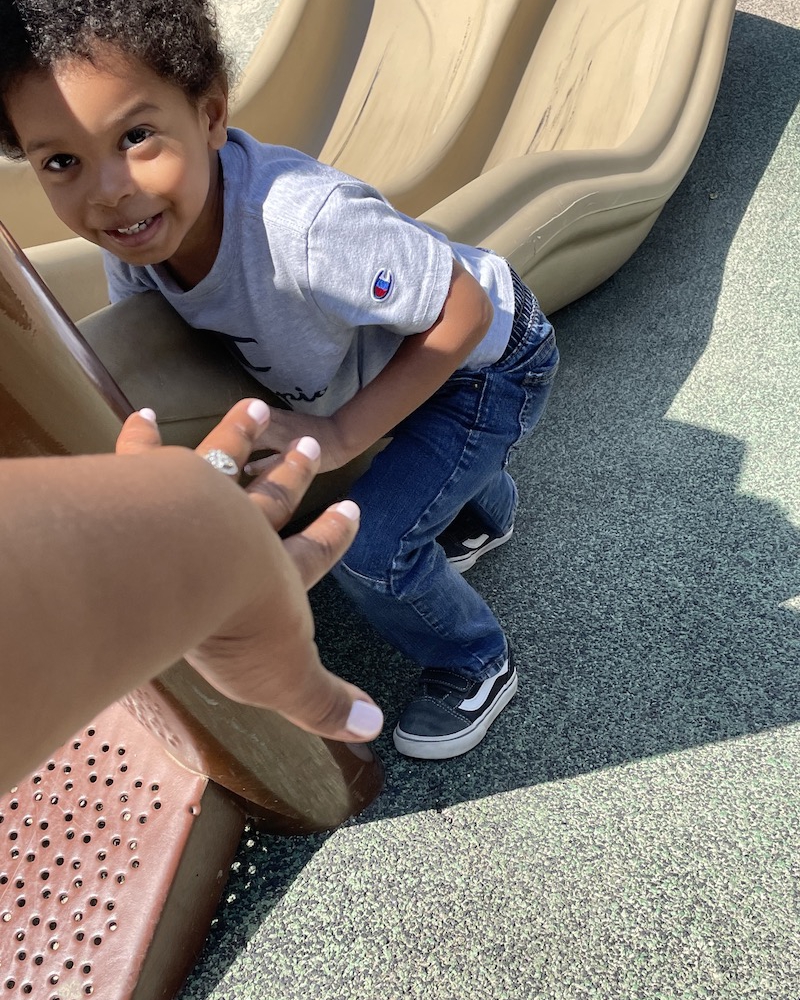 Ms. Tee is holding out her hand to help a little boy get on the slide.
