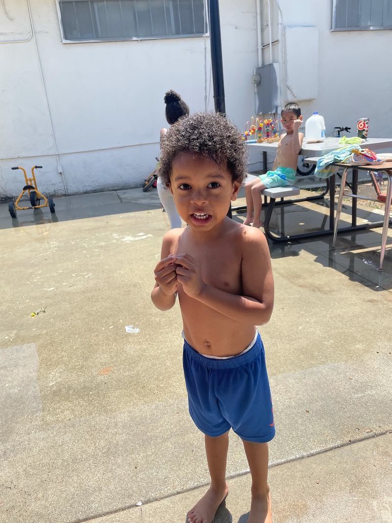A little boy is standing in the sun after playing in the pool.