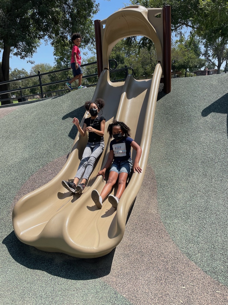 Two girls on the slide are having fun at the park.