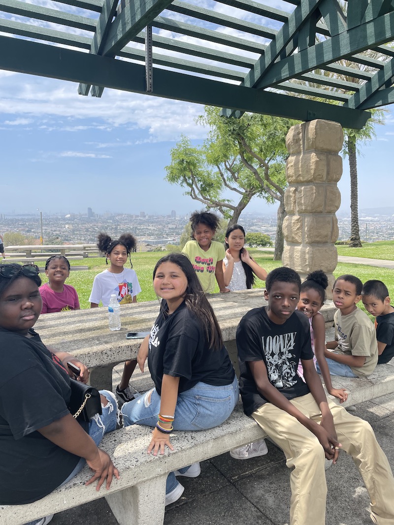 Kids are sitting at a picnic table at the park, smiling for a picture.