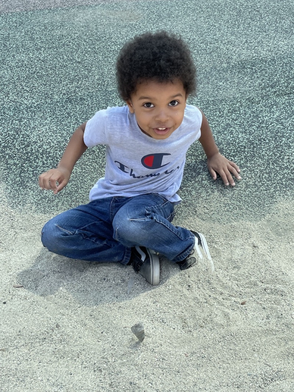 The little boy is digging his feet into the sand at the playground.