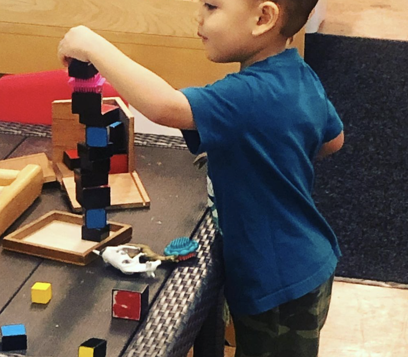 A boy is standing by a table playing with building blocks.