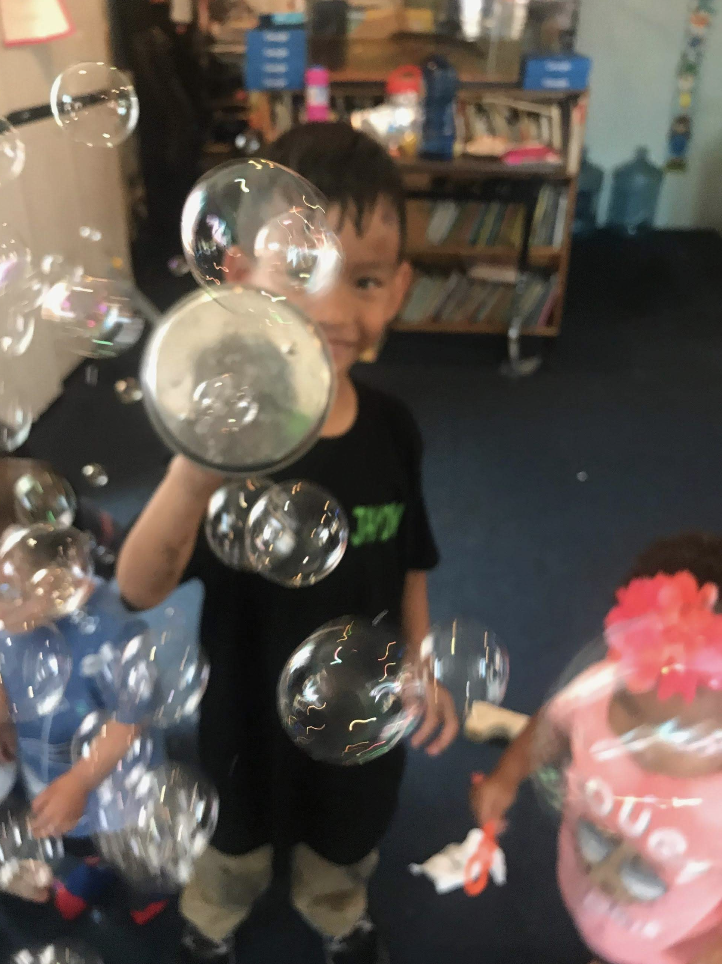 Smiling kids are blowing bubbles and popping them.