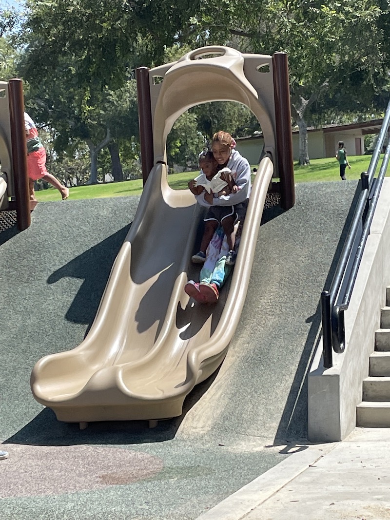 A little girl is being held by her teacher, sliding down the slide.