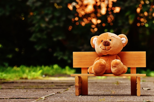A stuffed teddy bear is sitting on the bench in the park.
